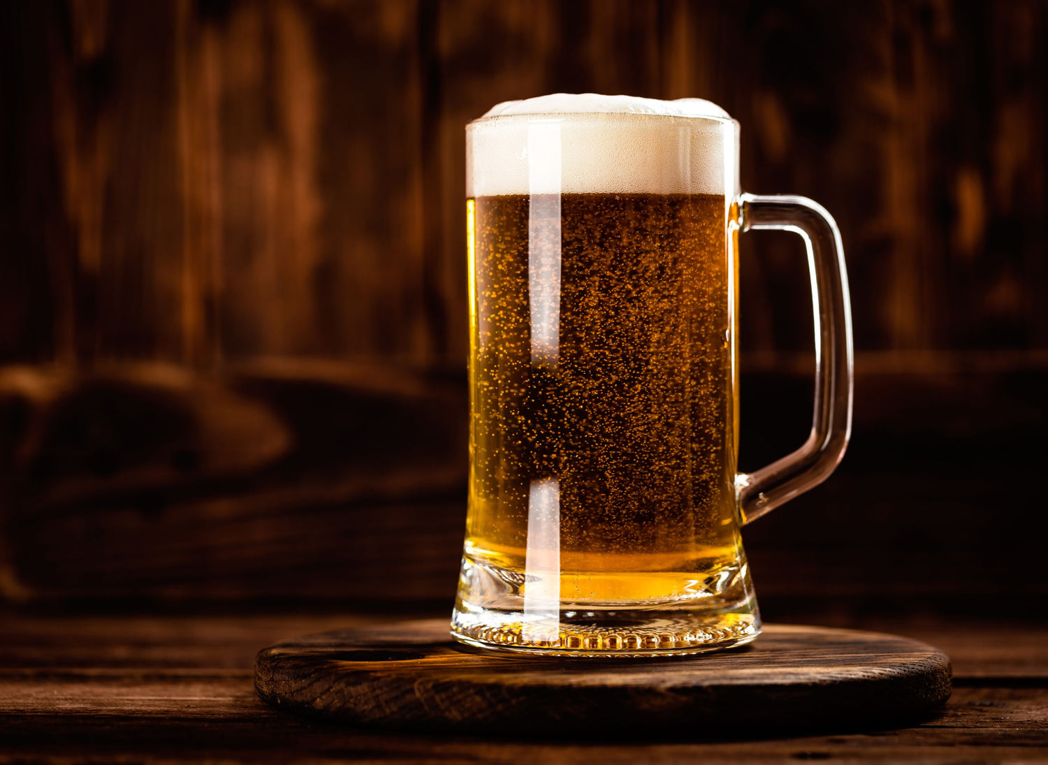 Bierglas mit Schaumkrone steht auf einem Holzbrett.